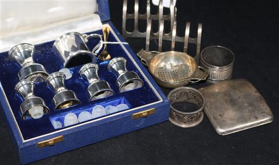 A cased silver condiment set, a pair of toast racks, two napkin rings, a tea strainer and a cigarette case